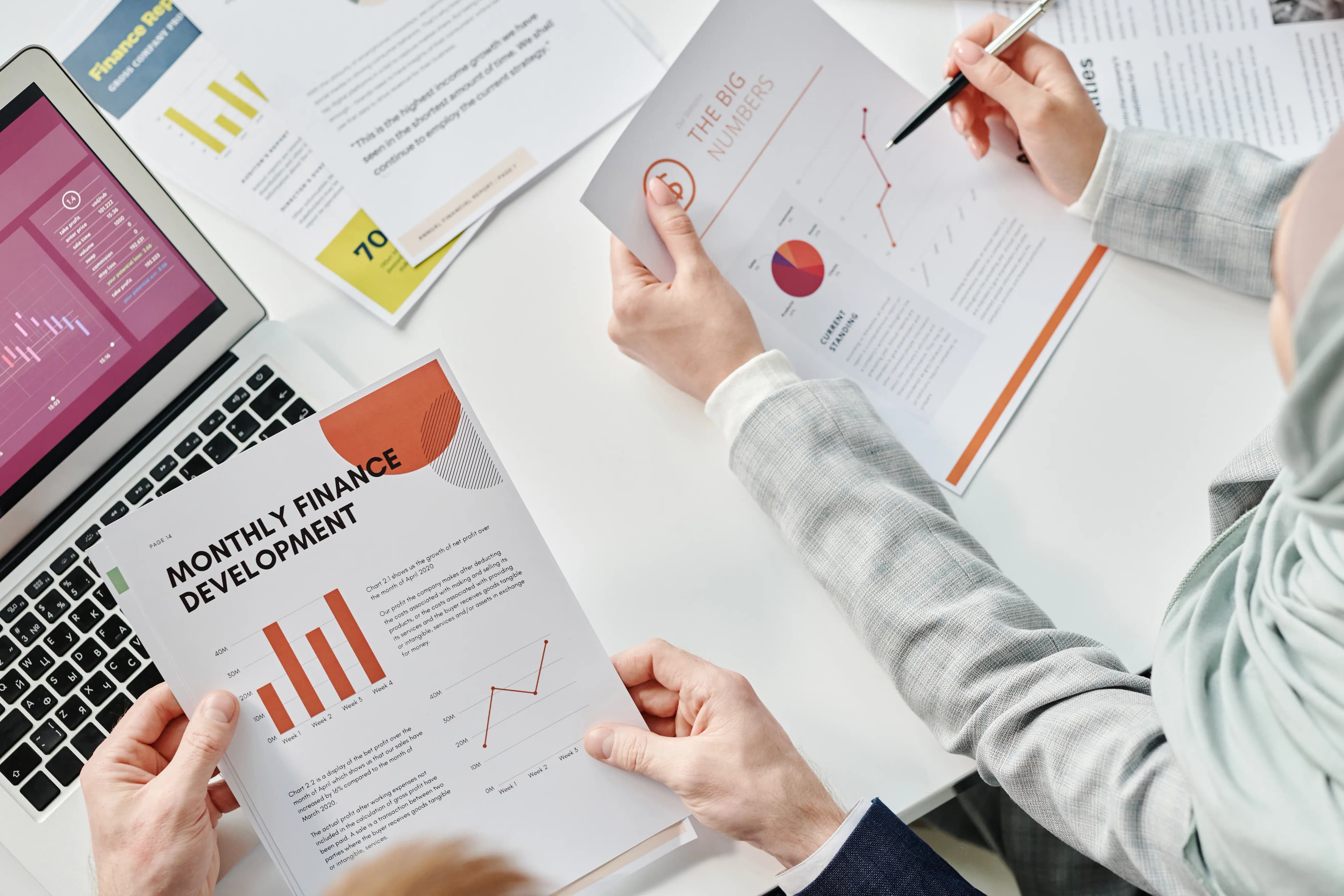 Dizüstü bilgisayar yanında grafikli raporu inceleyen kişi